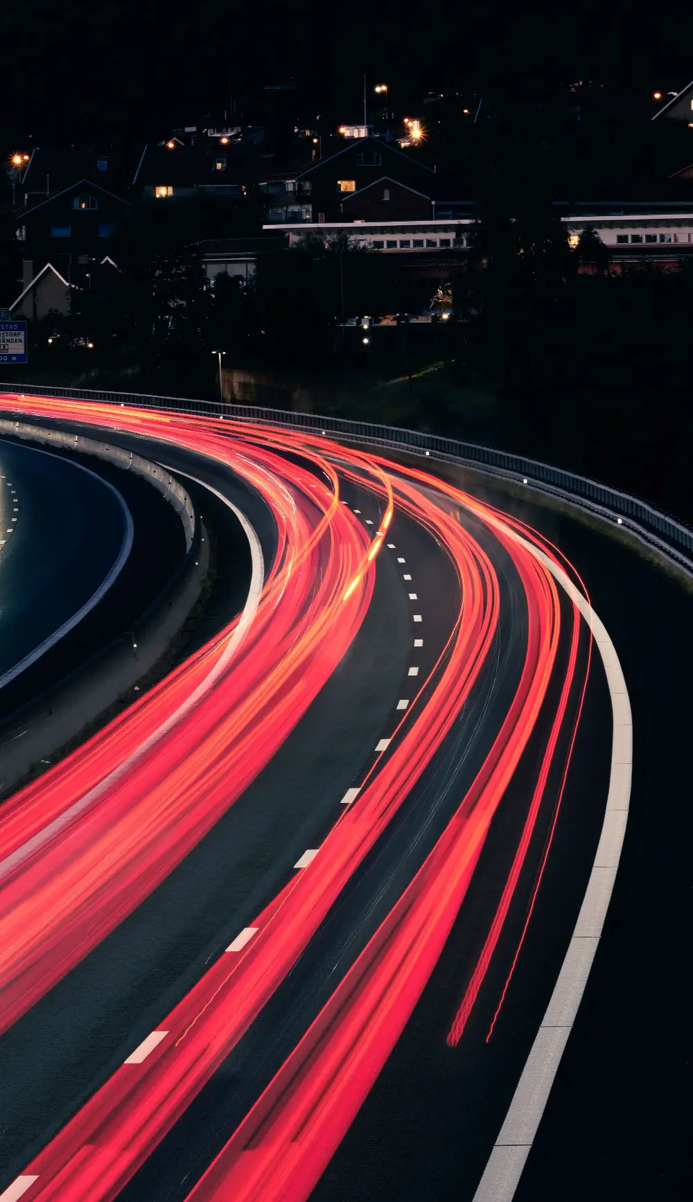 Rote Lichtspuren von Autos auf einer nächtlichen Autobahnkurve